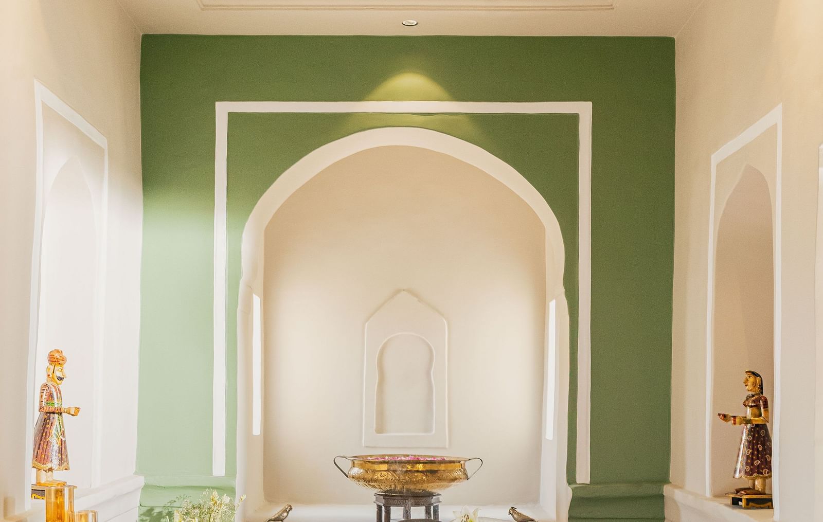 A serene spa treatment room with soft lighting, featuring a massage table, arched alcove, and calming green accents.