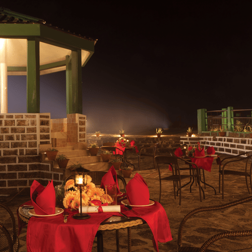 A spacious outdoor deck with seating and dining tables, surrounded by lush trees, at Polo Cherrapunjee Resort.