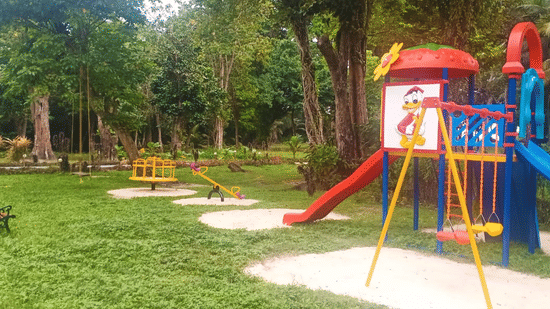 Children’s outdoor play area at Silver Sand Beach Resort Neil featuring colourful slides, swings, playground equipment, and green lawn surrounded by trees.
