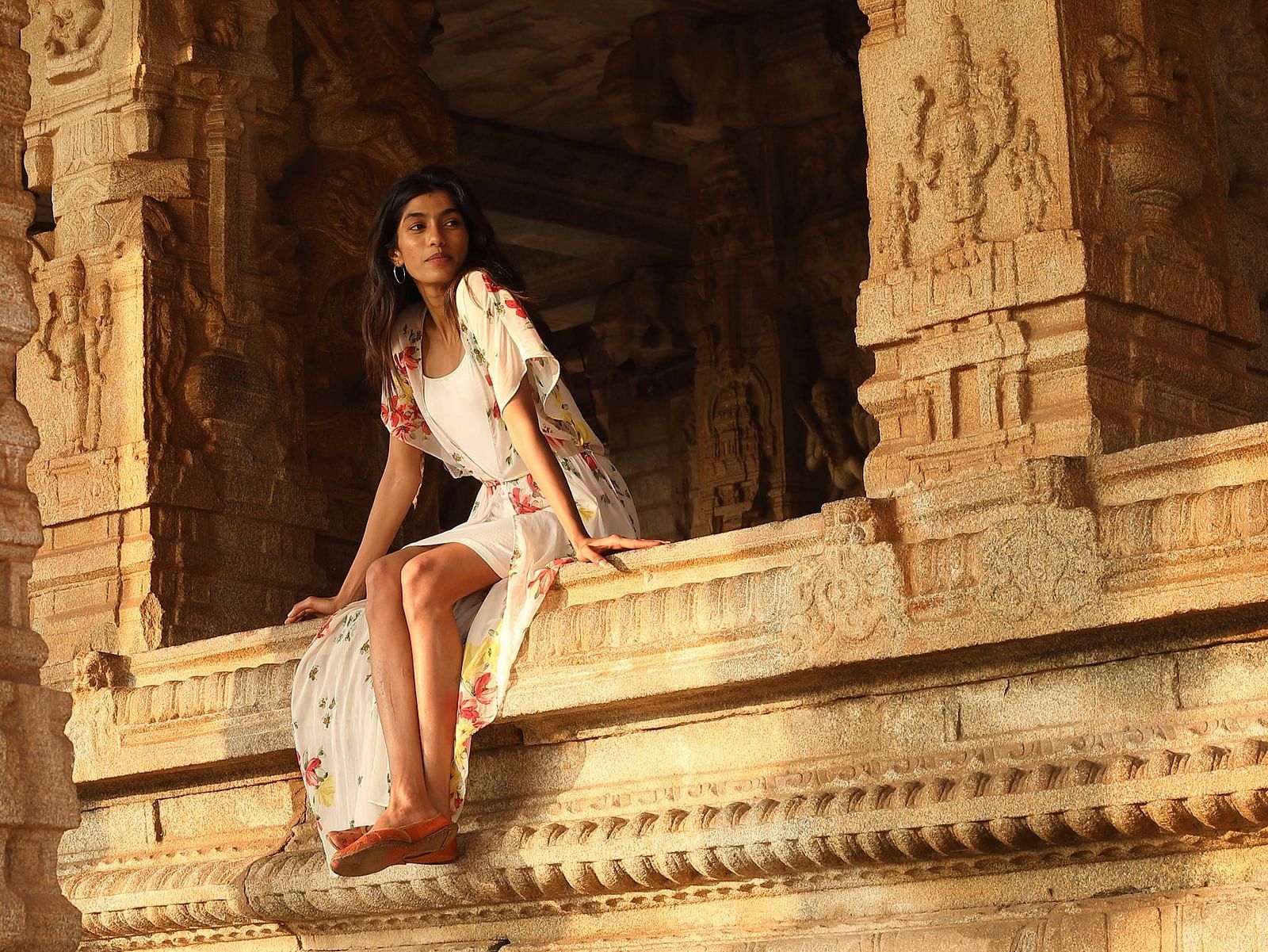 Person in a floral dress sitting on ancient Hampi temple steps.