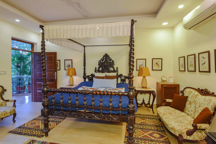A room at the Shaheen Bagh resort featuring a plush wooden bed, wooden chairs, side tables, and a door leading to the balcony.