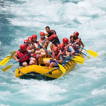 A group of people rafting, while wearing safety jackets andholding paddles on a river