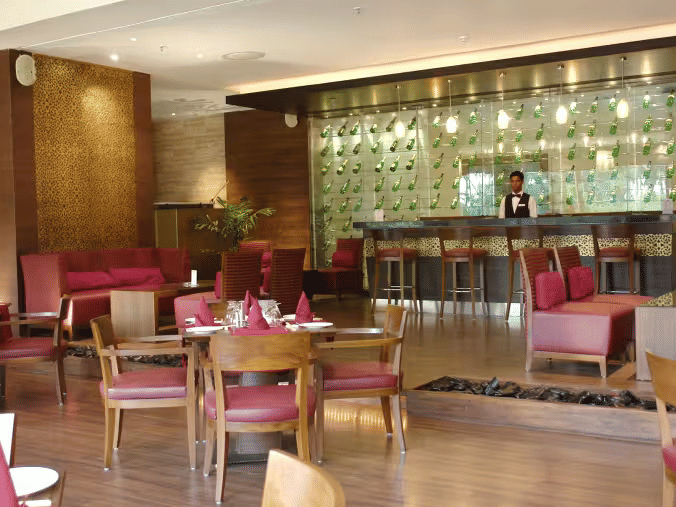 Restaurant dining area at Retreat with wooden chairs and pink upholstered seating arranged around tables with a backlit bar counter and decorative wall panels visible in the background.
