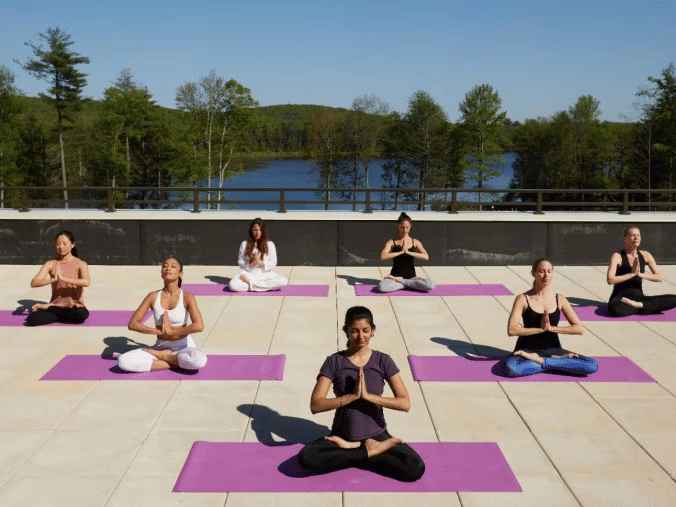 A group of 7 people on yoga mat meditating on a rooftop with a lush background at YO1 Longevity and Health Resorts, Catskills