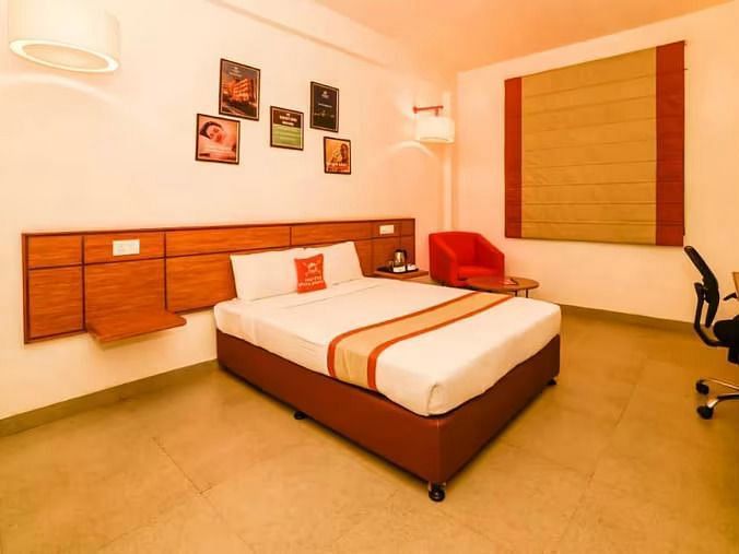 Well-lit hotel room with a double bed, wooden furniture, and wall art - Max Hotel Prayagraj