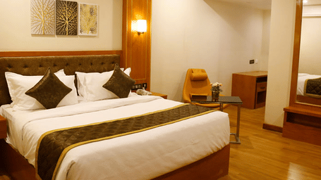 A double bed with a brown bed runner spread over it at the Deluxe Room featuring a glossy wooden flooring at Leroy Grand, Yeshwanthpur.