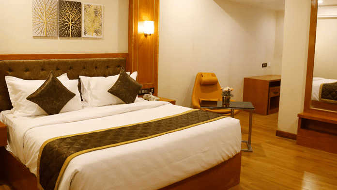 A double bed with a brown bed runner spread over it at the Deluxe Room featuring a glossy wooden flooring at Leroy Grand, Yeshwanthpur.