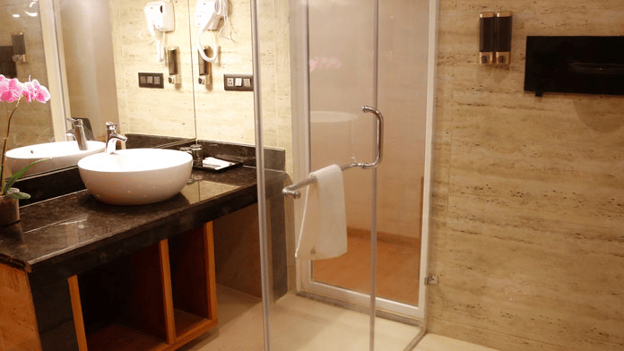 The vanity area of in the bathroom of the Deluxe Room along with a glass door separating the shower cubicle at Leroy Grand, Yeshwanthpur.