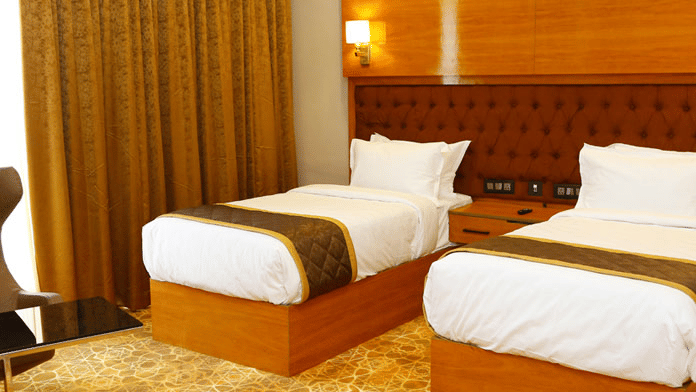 Neatly kept twin beds at the Executive Room with blackout curtains covering the window beside it at Leroy Grand, Yeshwanthpur.