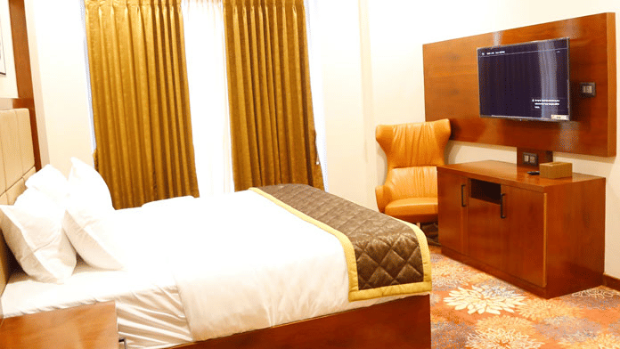 Side angle view of the Family Suite featuring a plush double bed facing a wall-mounted television with an armchair placed in the corner at Leroy Grand, Yeshwanthpur.