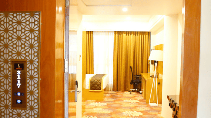 The entrance of the Family Suite at Leroy Grand, Yeshwanthpur, featuring a carpeted flooring and the corner of the bed with a work station in front of it visible from the entrance.