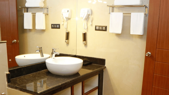 The bathroom at the Family Suite featuring a wash basin with a huge mirror and a hair dryer mounted to the tiled wall at Leroy Grand, Yeshwanthpur.