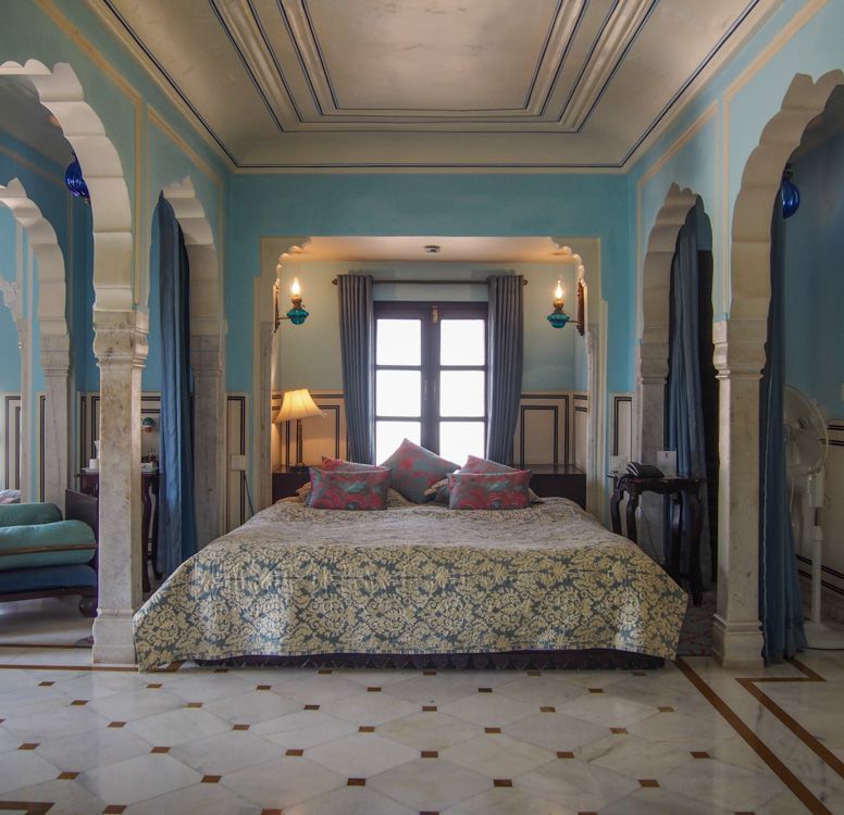 A bedroom at Royal Heritage Haveli featuring a large bed with a patterned cover, blue walls, and arched architectural details.