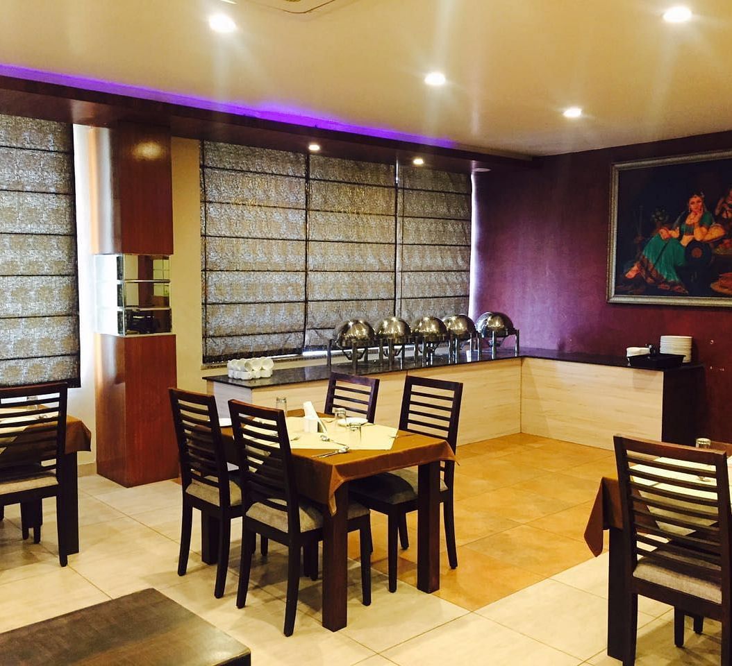 A dining room with a serene ambience, featuring a mix of wooden chairs and tables and a decorative screen - TGI Apple Inn, Jaipur 