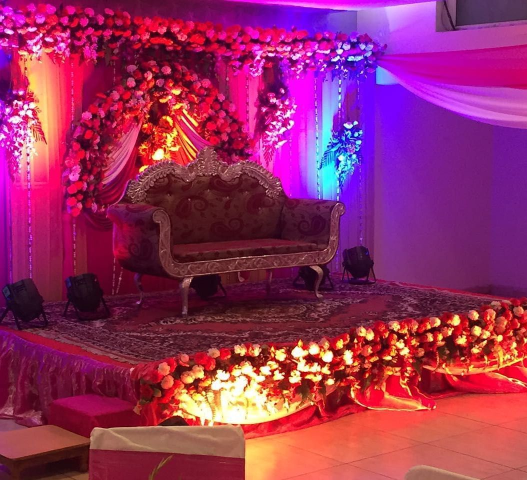 A wedding stage with red and white floral arrangements and a couch under a spotlight - TGI Apple Inn, Jaipur 