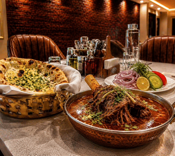 Dining table at Lime Tree Hotel & Banquet, Jaipur, with a bowl of meat curry, a basket of naan and a side salad.