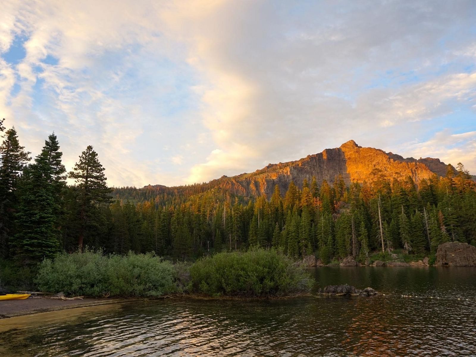 A sunset casts warm light on a mountain peak surrounded by a forest and a body of water