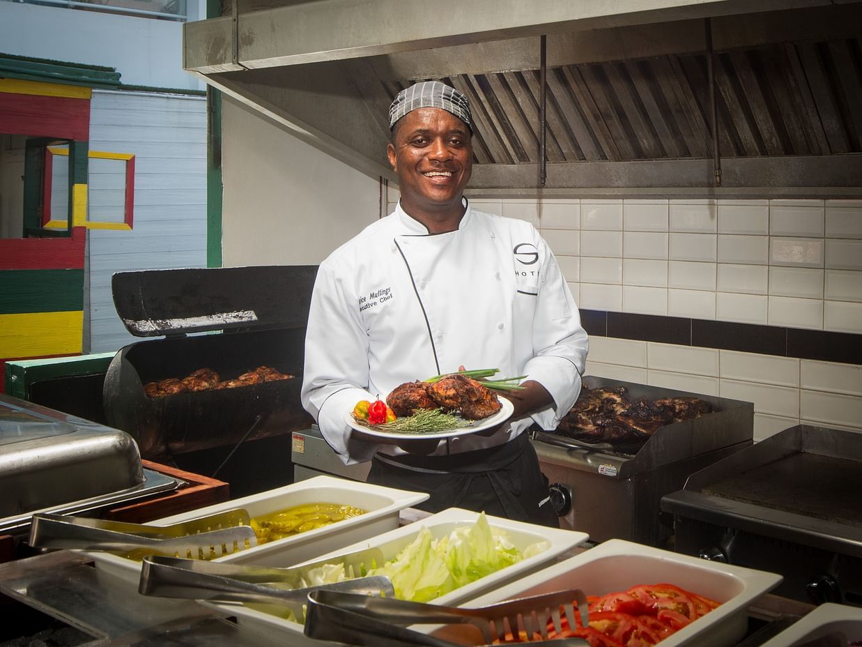 A chef holding a plate of grilled food in a kitchen  - S Hotel Montego Bay, Jamaica