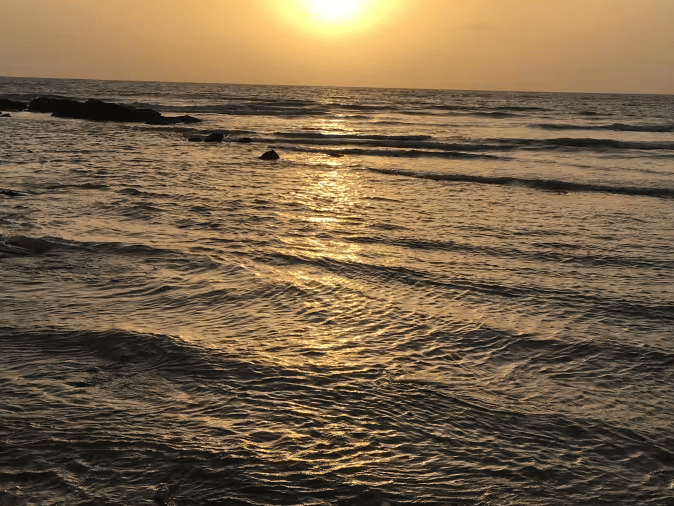 A sunset view over the sea with waves approaching the shore.