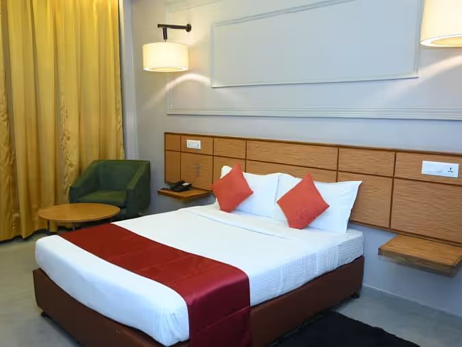 A well-designed hotel room with two beds, modern lighting, and a cosy seating area - Max Hotel Prayagraj.