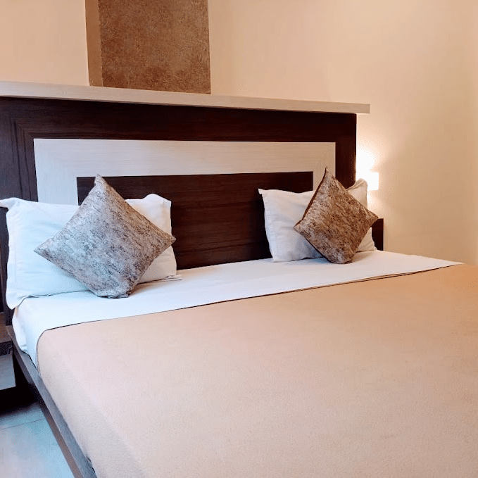 Cozy double bed set with light brown linens, plump white pillows, patterned accent cushions, and bedside tables.
