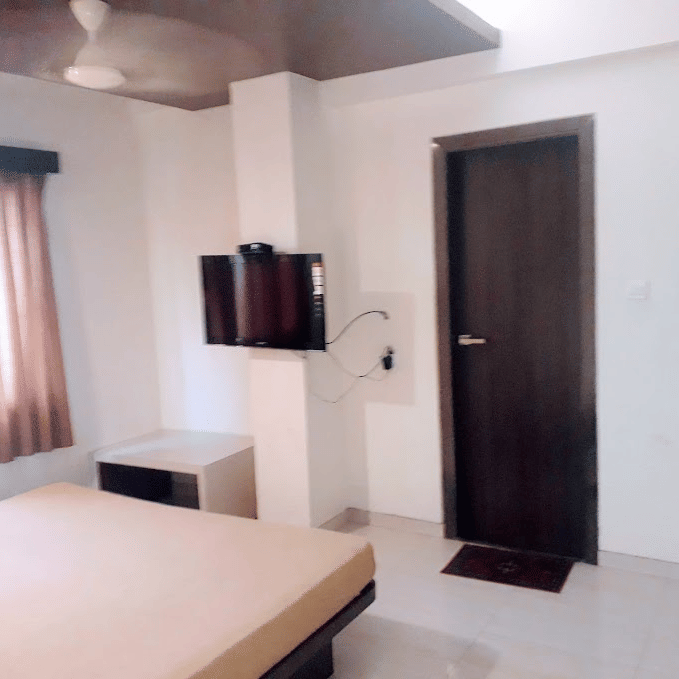Deluxe room featuring a double bed with a light beige runner, an entry door, and a tall wooden wardrobe.
