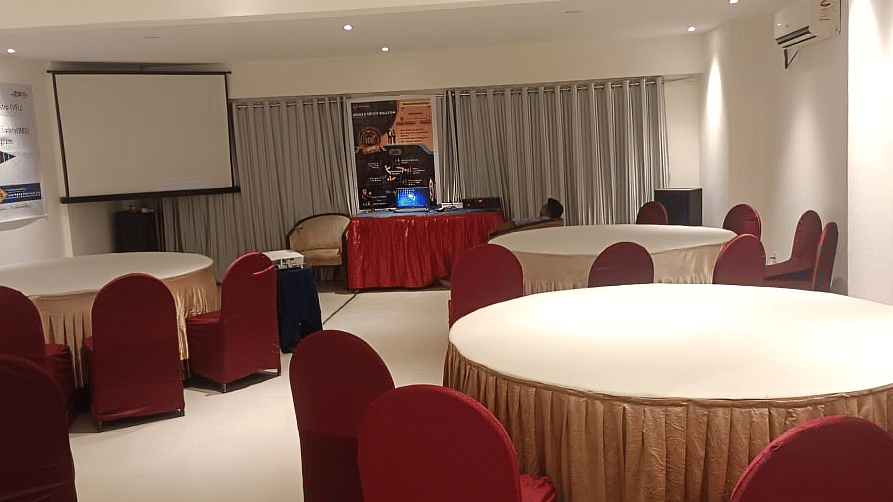 Professional banquet hall at Lords Eco Inn Dahej with round tables, burgundy chairs, and presentation screen for events and conferences