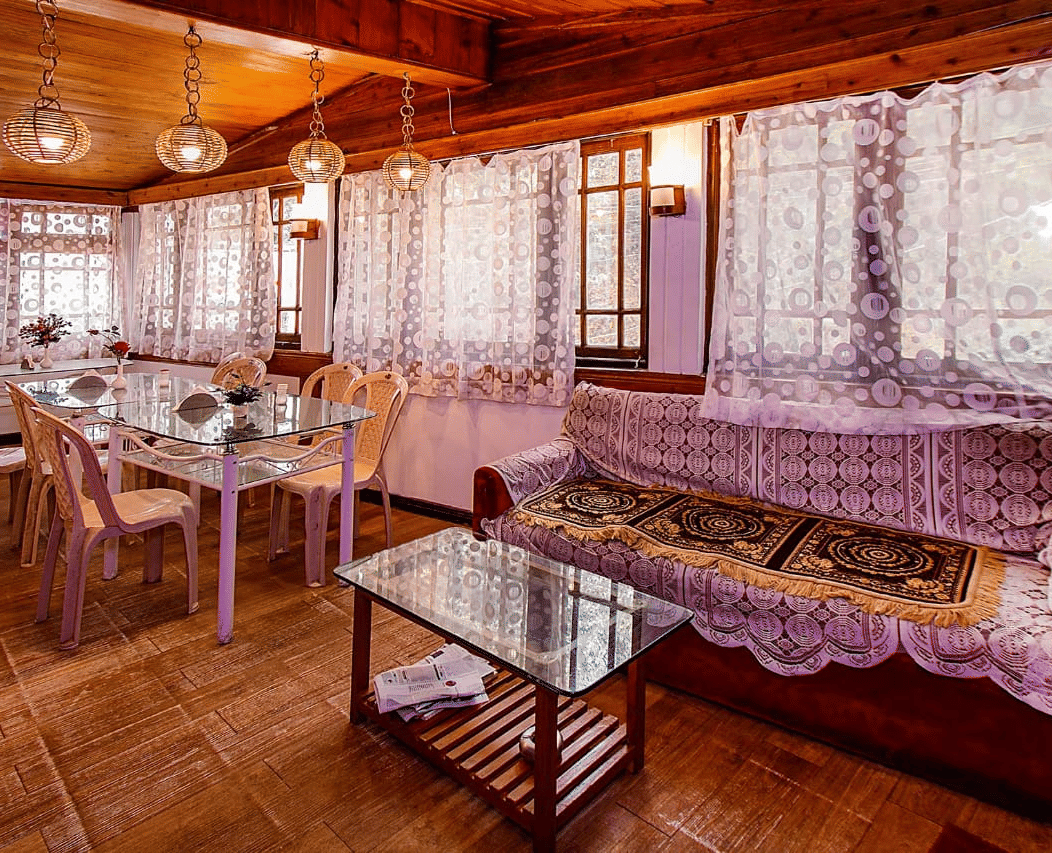 Restaurant/dining room with lace curtains, wooden walls and ceiling, glass tables, and light-coloured chairs at Hotel Dolphin Darjeeling.