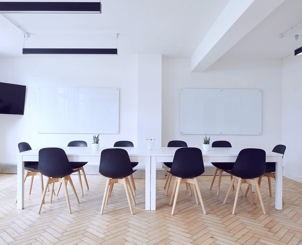 A meeting room with chairs arranged around a table with 2 whiteboards in the background.