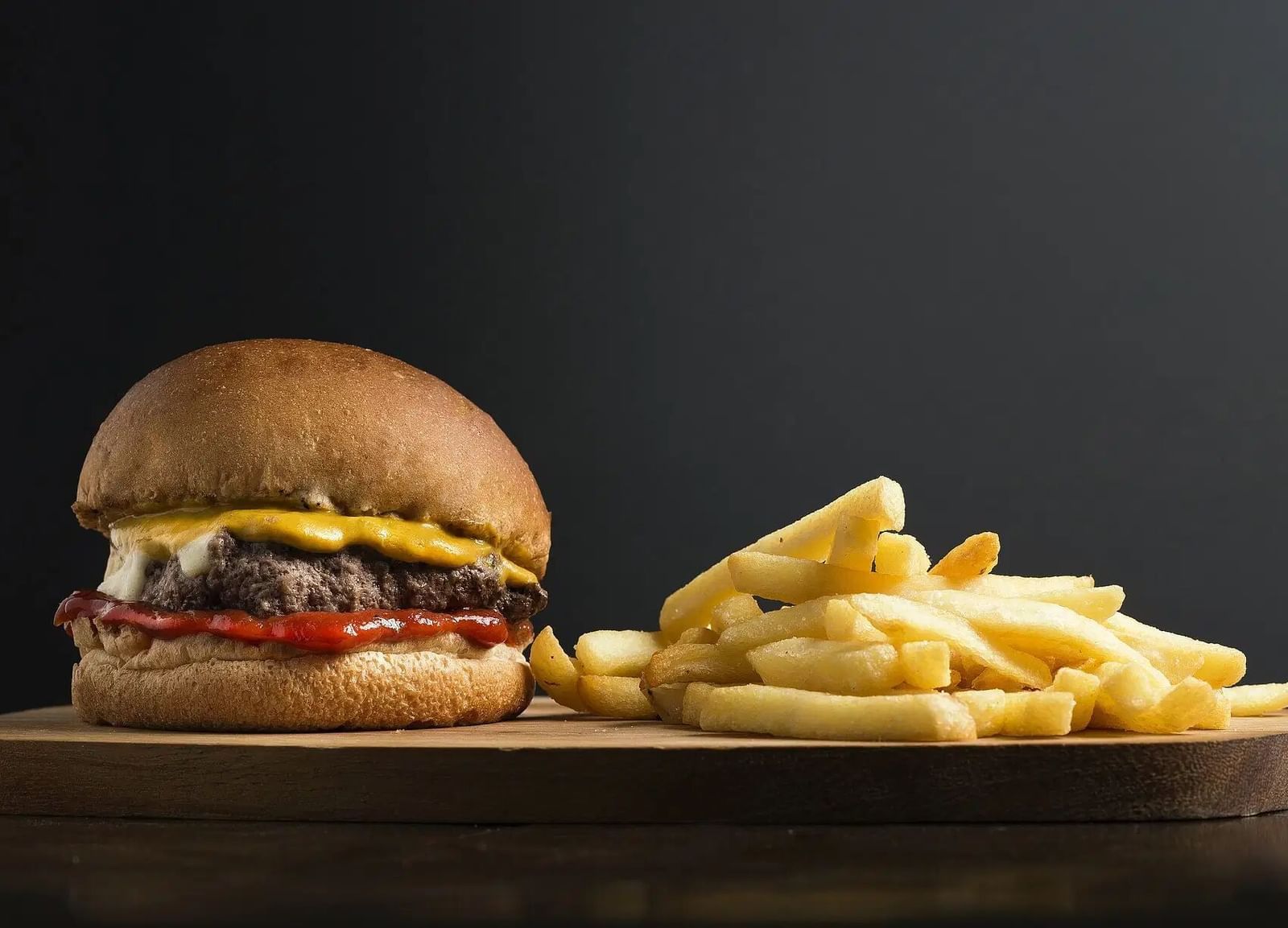 A classic cheeseburger served with a side of golden french fries on a dark background | Altamont Court, Jamaica
