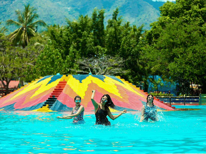 People splashing and enjoying in a swimming pool at Black Thunder surrounded by lush green trees in the background, one of the best Fun Activities in Coimbatore.