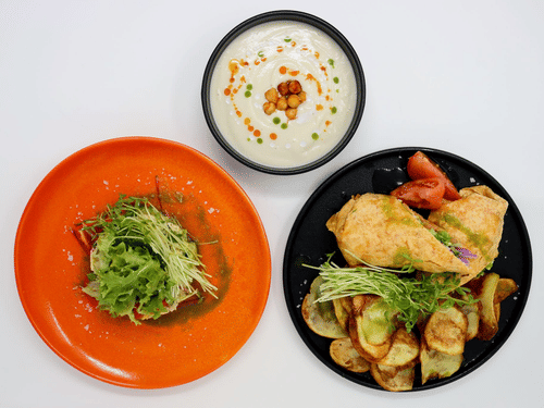 Three colorful plates of food on a white surface, featuring a creamy soup, leafy salad, and a main dish with vegetables at YO1 Longevity and Health Resorts, Catskills