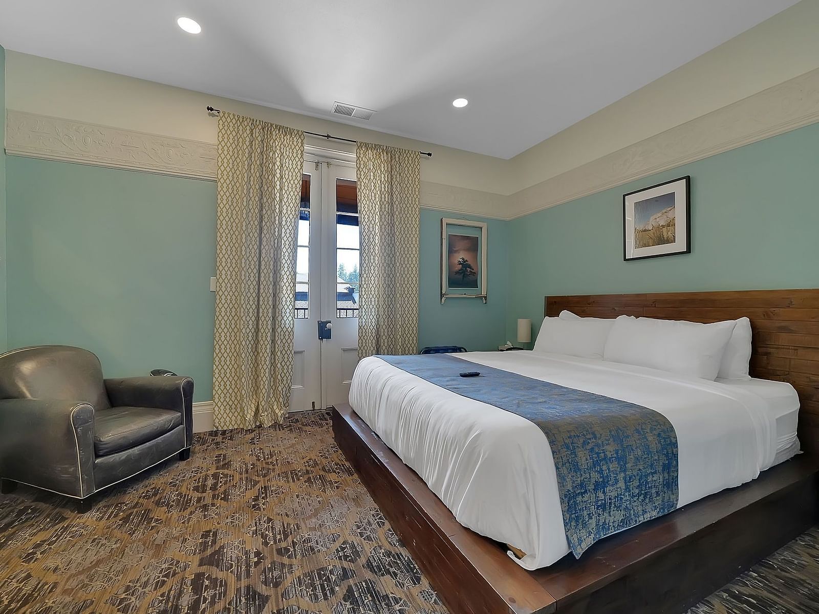 a room at The Groveland Hotel with a wooden double bed, an armchair, and the door to a balcony.