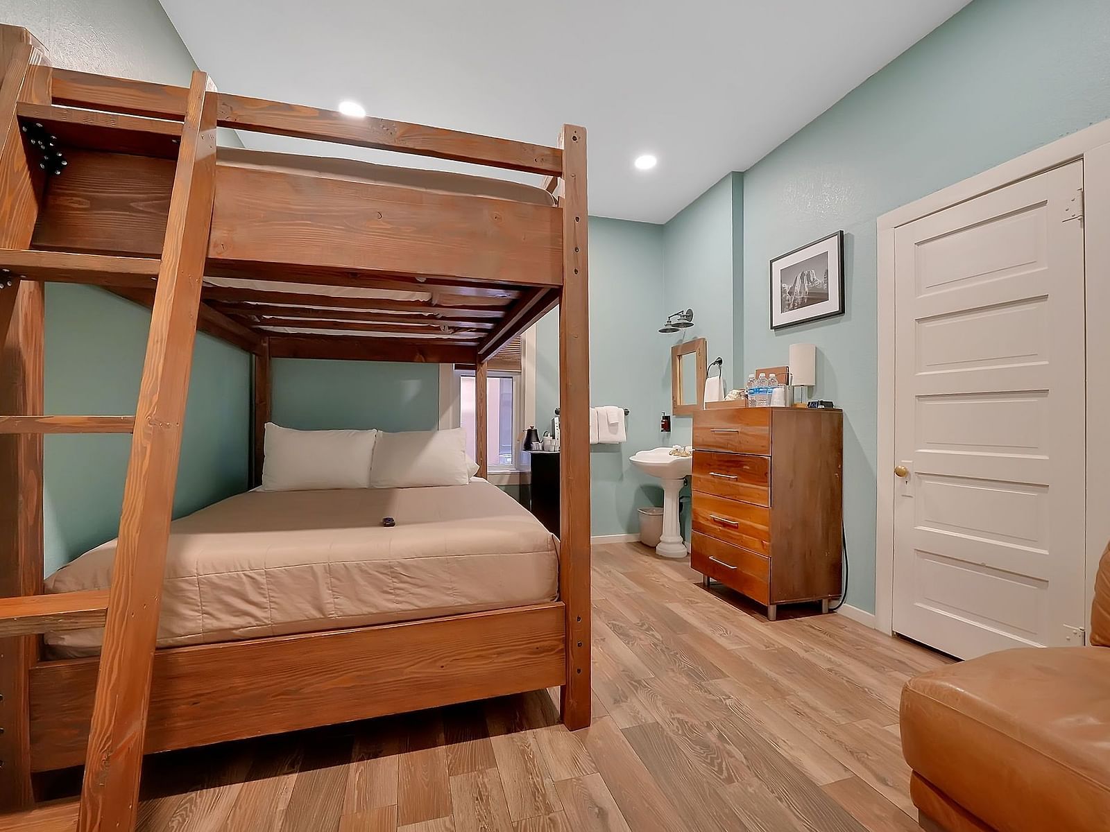 interior of a room at The Groveland Hotel with wooden bunk beds, a leather sofa and a dresser in view.