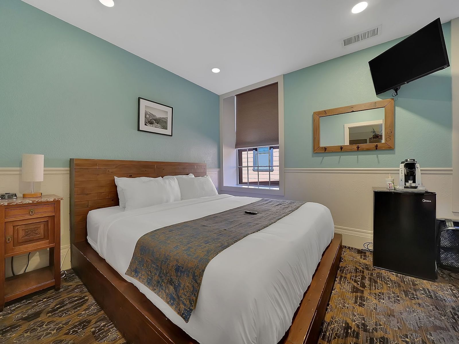 A comfortable room at The Groveland Hotel with sage green walls, wooden bed, blue patterned runner, TV, and convenient coffee station.