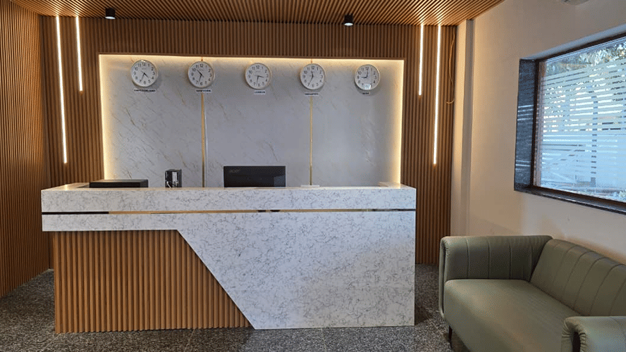Side view of a white front desk counter with wall lights and a green couch placed nearby for waiting guests.