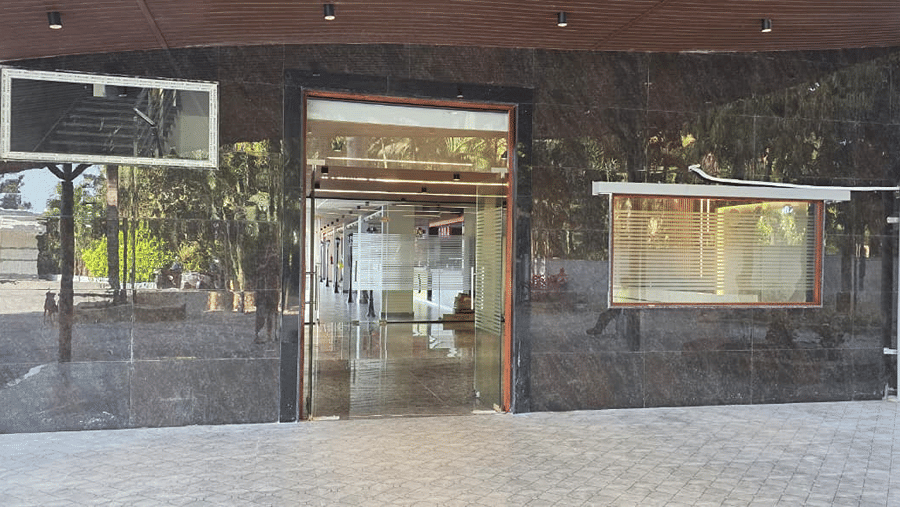 Glass entrance doors leading into the building, with a paved walkway and trees lining the path outside.