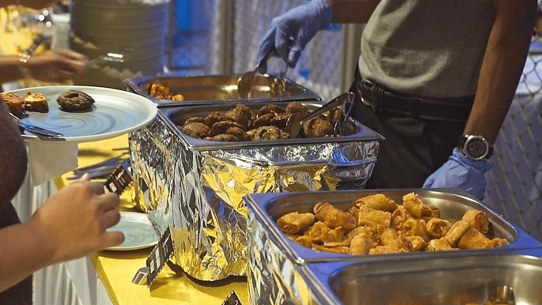 Close-up of hands serving food from chafing dishes onto plates at a buffet.