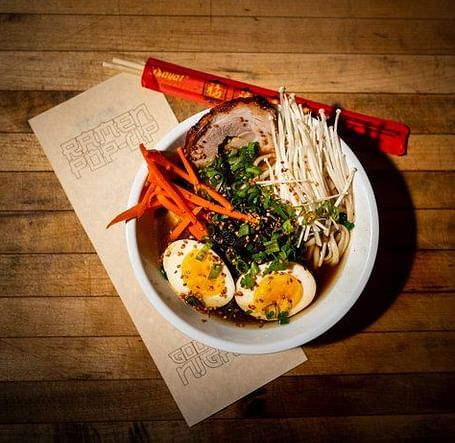 Overhead shot of a bowl with food and chopsticks on a wooden table. 