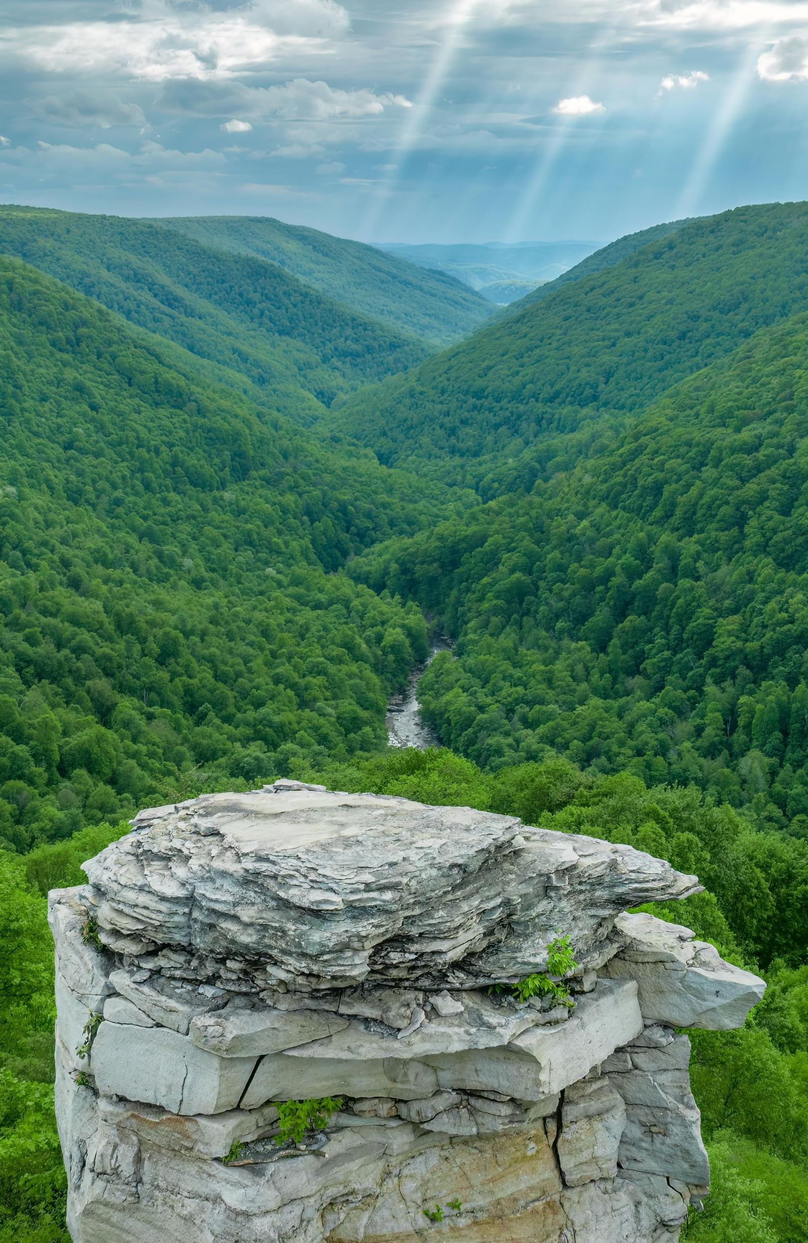 A rock structure overlooking a lush green valley on a cloudy day