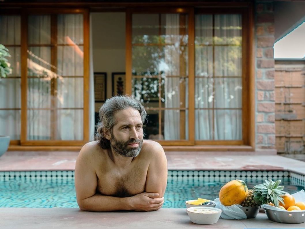 A man standing on a swimming pool with an assortment of fruits on the side at Surpura Bagh.