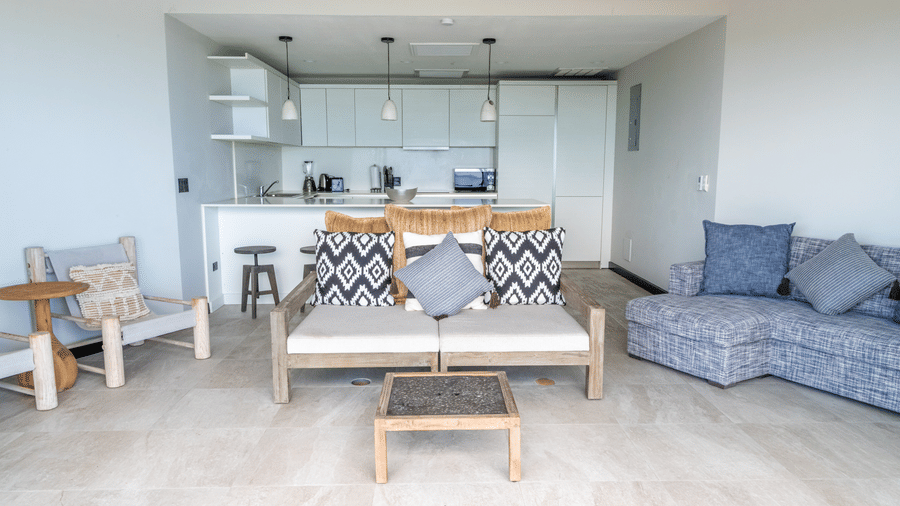 A living room at Tamarind Hills Resort and Villas, Antigua, with two sofas, two lounge chairs, and a table in front of a kitchen area.