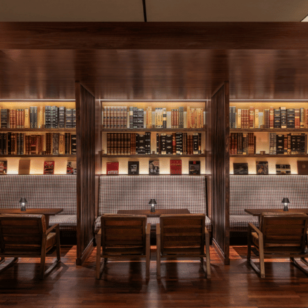 A cozy restaurant with wooden tables and chairs, and a wall lined with liquor bottles and books.