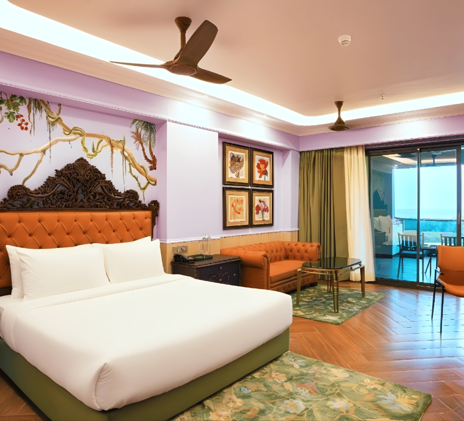 A brightly designed room featuring a double bed with upholstered headboard, floral mural, lounge chairs, balcony access and wooden flooring at MAYFAIR Bay Resort, Paradeep.