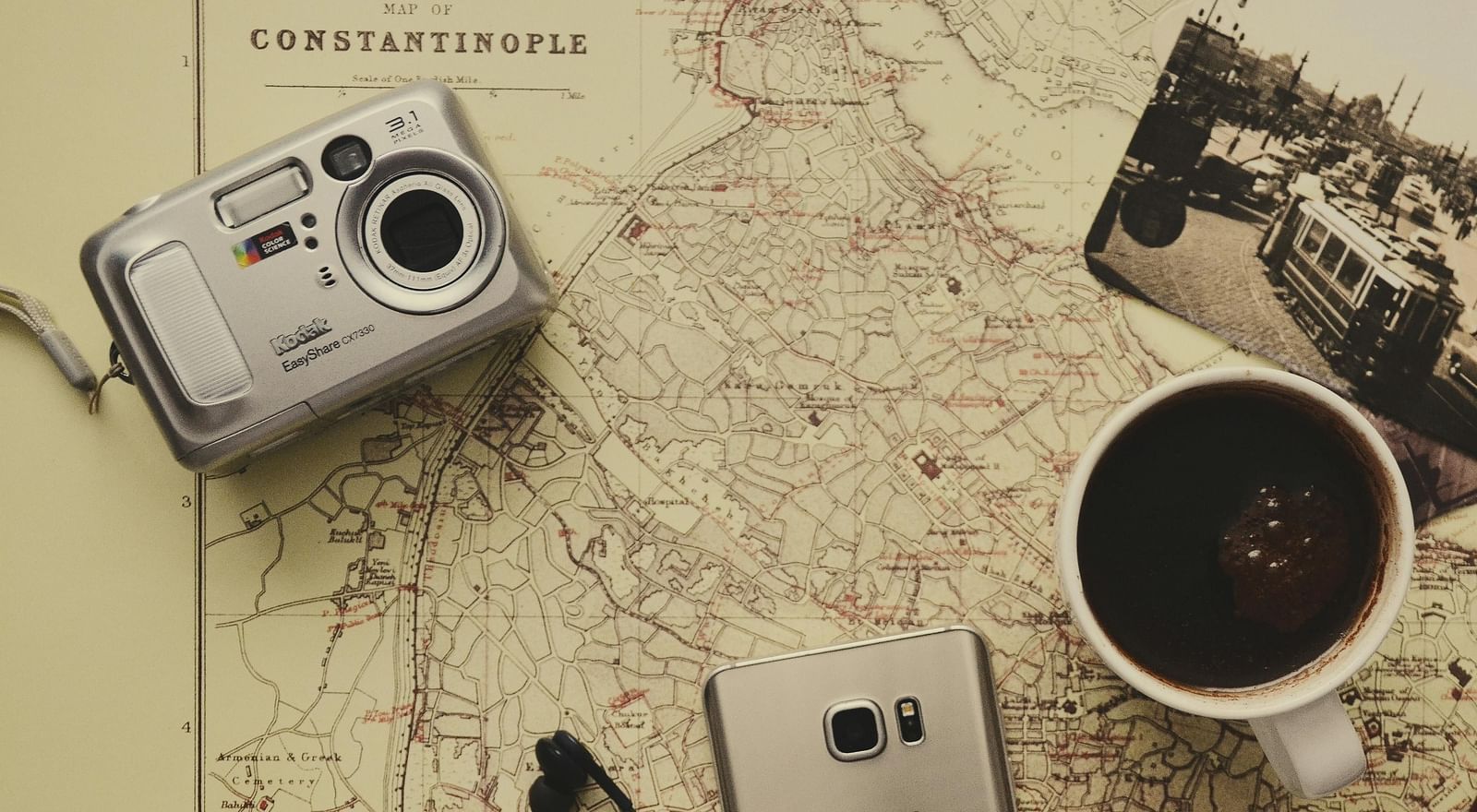 An image of a table laid our with a map, camera, phone, passport, photograph, and coffee