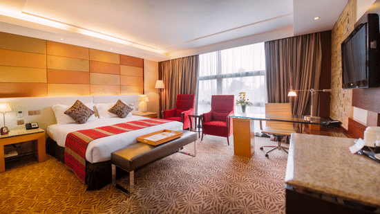 Superior Room at The Boma Nairobi featuring a bed with a red runner, a lounge area, and a desk in front of a window