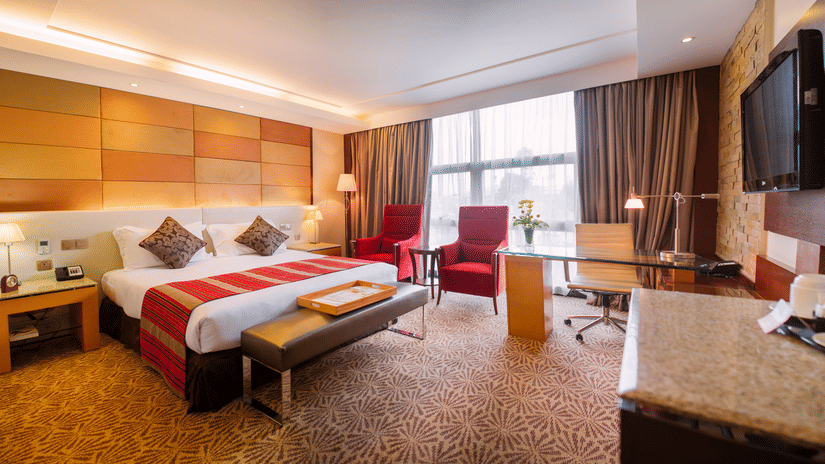 Superior Room at The Boma Nairobi featuring a bed with a red runner, a lounge area, and a desk in front of a window