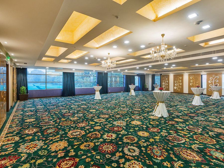 Spacious event hall with a patterned green carpet, elegant chandeliers, and draped cocktail tables - Heritage Village Resorts & Spa.