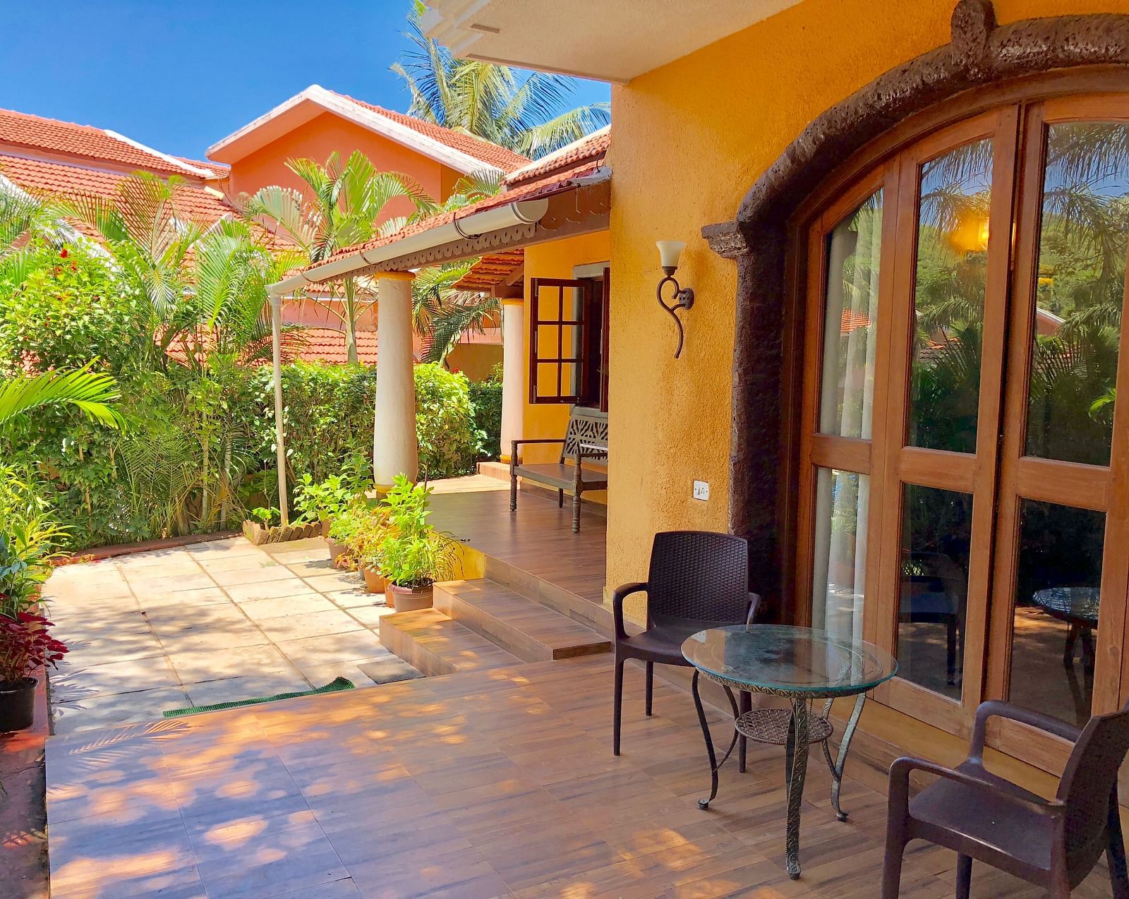Exterior sitting area during daytime at The Bungalows Light House, Goa featuring a coffee table and a pair of chairs with lush greenery in the surroundings