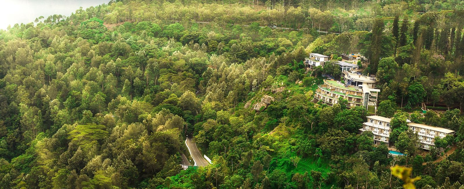 Drone shot of the hotel surrounded by mountains with sun light hitting the lush greenery - Great Trails Yercaud by GRT Hotels